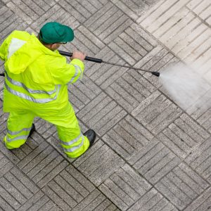 Worker cleaning a pavement sidewalk with high pressure water jet. Maintenance of public areas